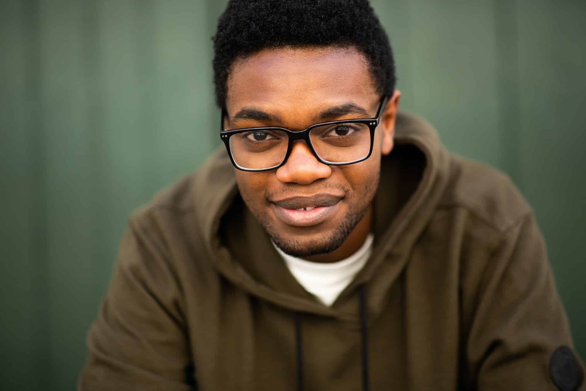 Close up young black man with glasses by green wall